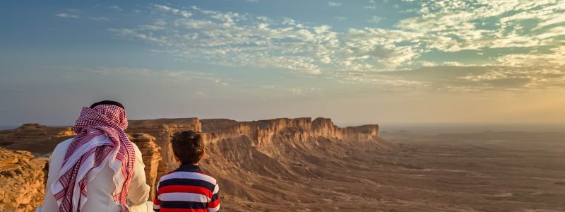 An arab man and his son sitting in Edge of the world, a natural landmark and popular tourist destination near Riyadh -Saudi Arabia.08-Nov-2019. Selective focus and background blurred.