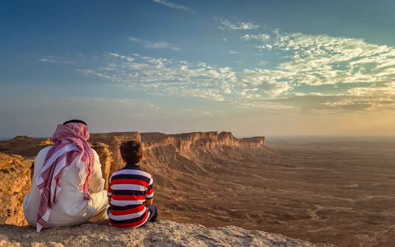 An arab man and his son sitting in Edge of the world, a natural landmark and popular tourist destination near Riyadh -Saudi Arabia.08-Nov-2019. Selective focus and background blurred.